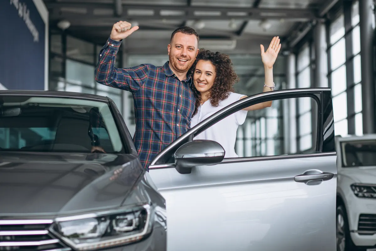 Casal comemorando ao lado do carro recém-adquirido